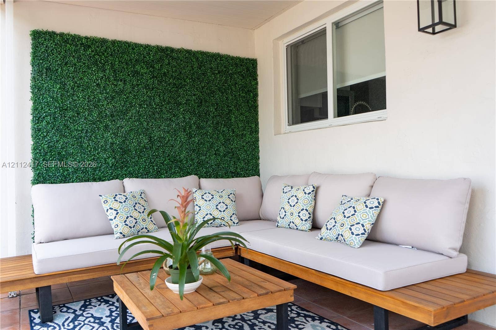 Covered patio featuring an artificial greenery accent wall, sliding window, and terracotta-toned tiled flooring