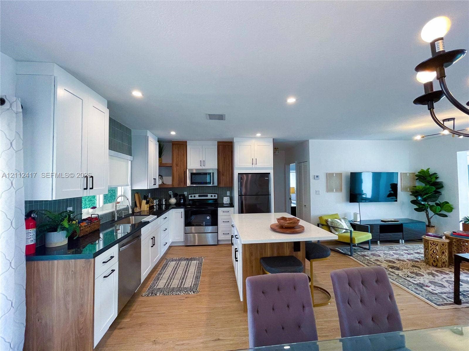 Kitchen featuring dual-tone cabinetry, central island with seating space, stainless steel appliances, dark countertops, and wood-finish flooring