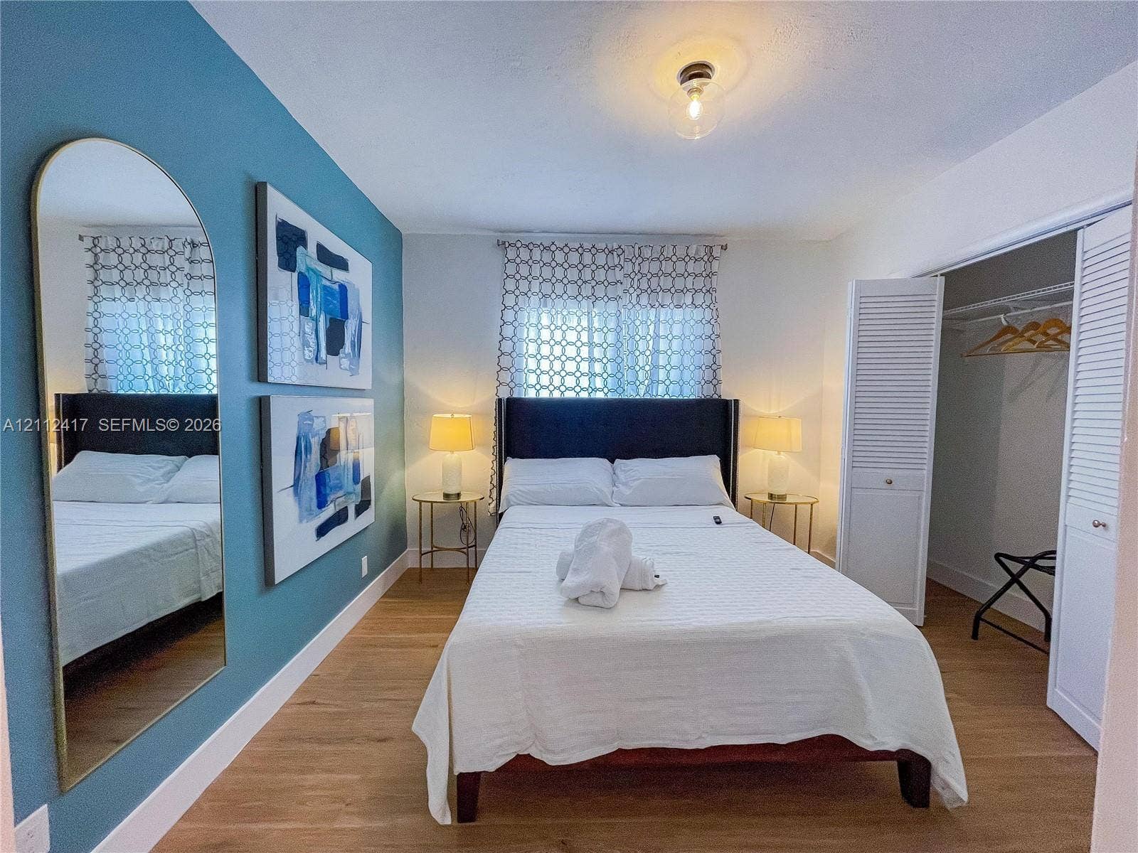 Room featuring wood-finish flooring, an accent wall, and a closet with louvered bi-fold doors