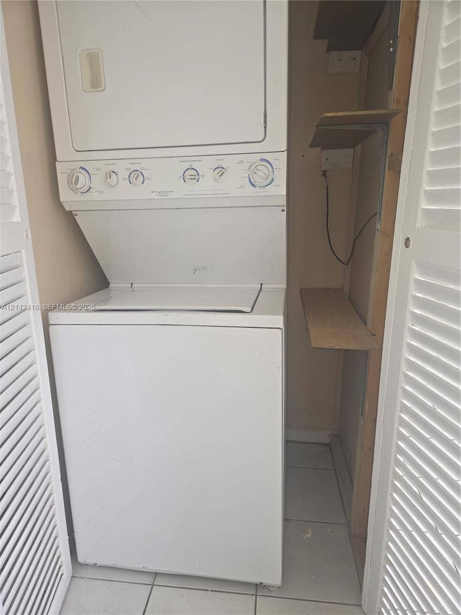 Stacked washer and dryer unit with louvered closet doors, tiled flooring, and built-in shelving