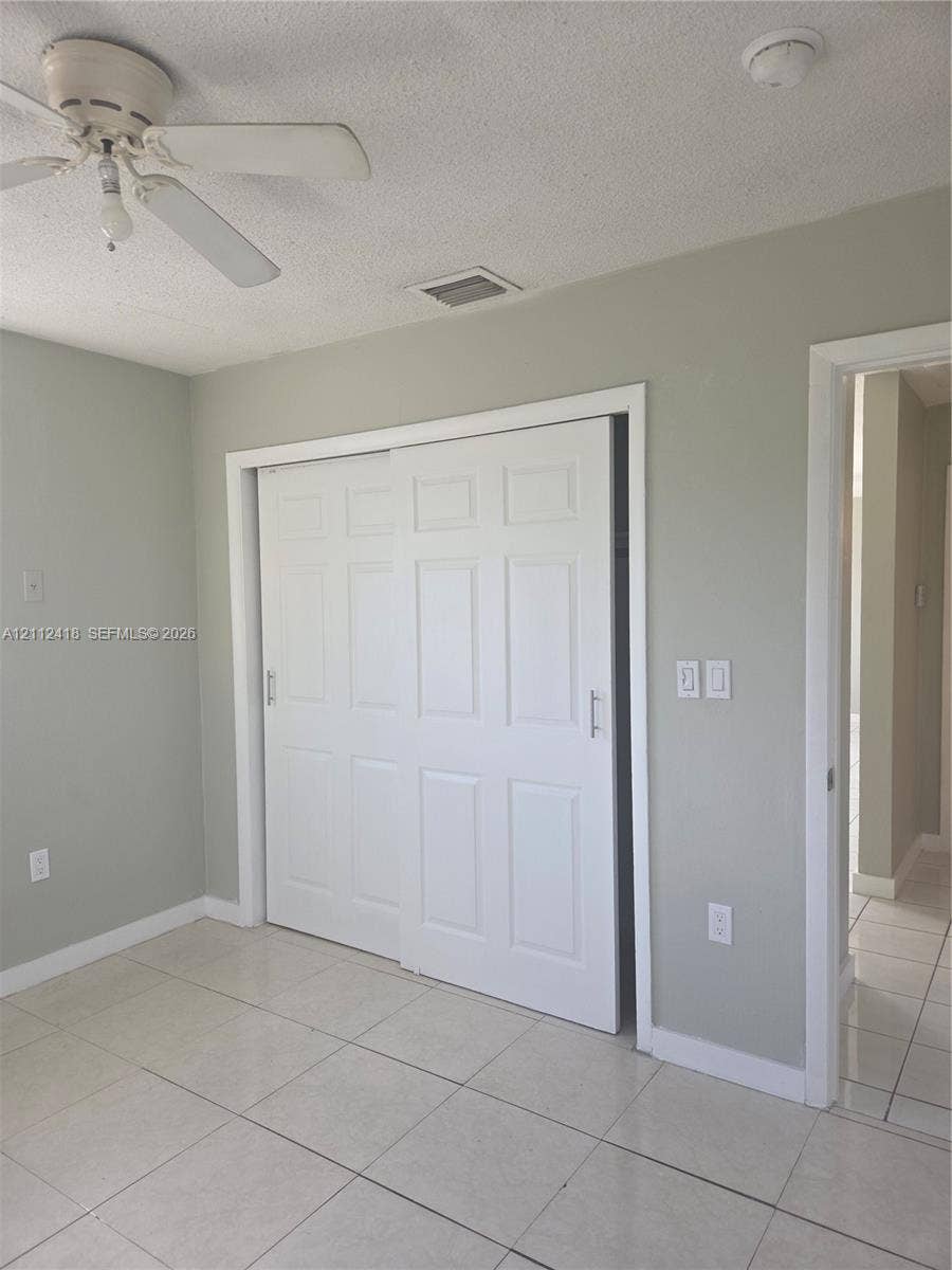 Neutral-toned interior space featuring light-colored tile flooring, six-panel sliding closet doors, and a ceiling-mounted fan with integrated lighting