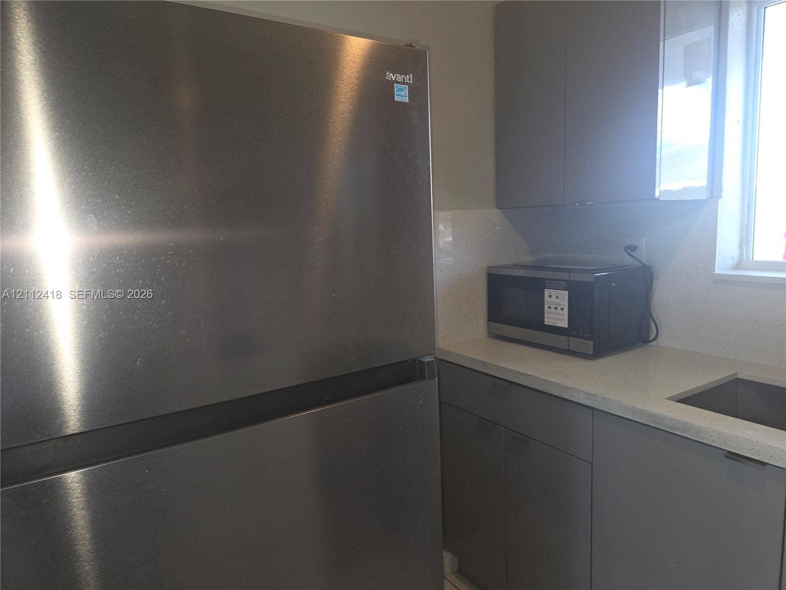 Stainless steel refrigerator, gray flat-panel cabinetry, light-toned stone-finish countertop, and undermount sink