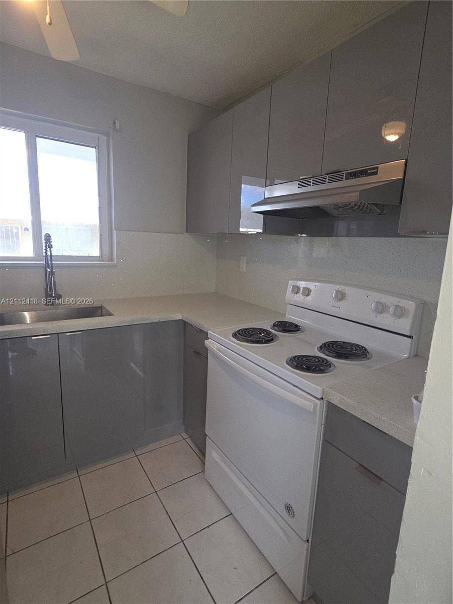 Kitchen featuring high-gloss grey cabinetry, stone-finish countertops, stainless steel undermount sink with a gooseneck faucet, white electric range, and tile flooring
