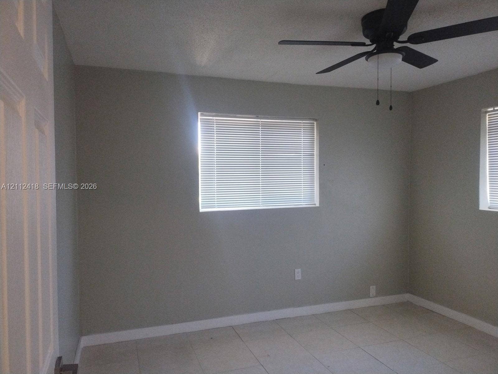 Neutral-toned walls featuring tile flooring, horizontal window blinds, and a multi-blade ceiling fan with integrated lighting