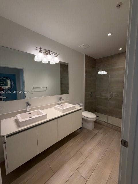 Dual-sink vanity with rectangular vessel basins, stone-finish countertop, frameless glass-enclosed shower featuring stone-tile surround, and wood-finish flooring