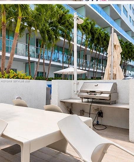 Outdoor terrace featuring a built-in stainless steel grill, stone-finish countertop, tile flooring, and perimeter privacy walls