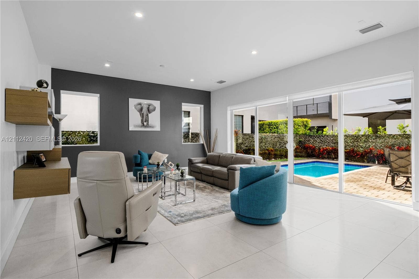10054 NW 76th Terrace, Doral, FL 33178 Open-concept living space featuring large-format tile flooring, a charcoal accent wall, recessed lighting, and wall-mounted wooden cabinetry