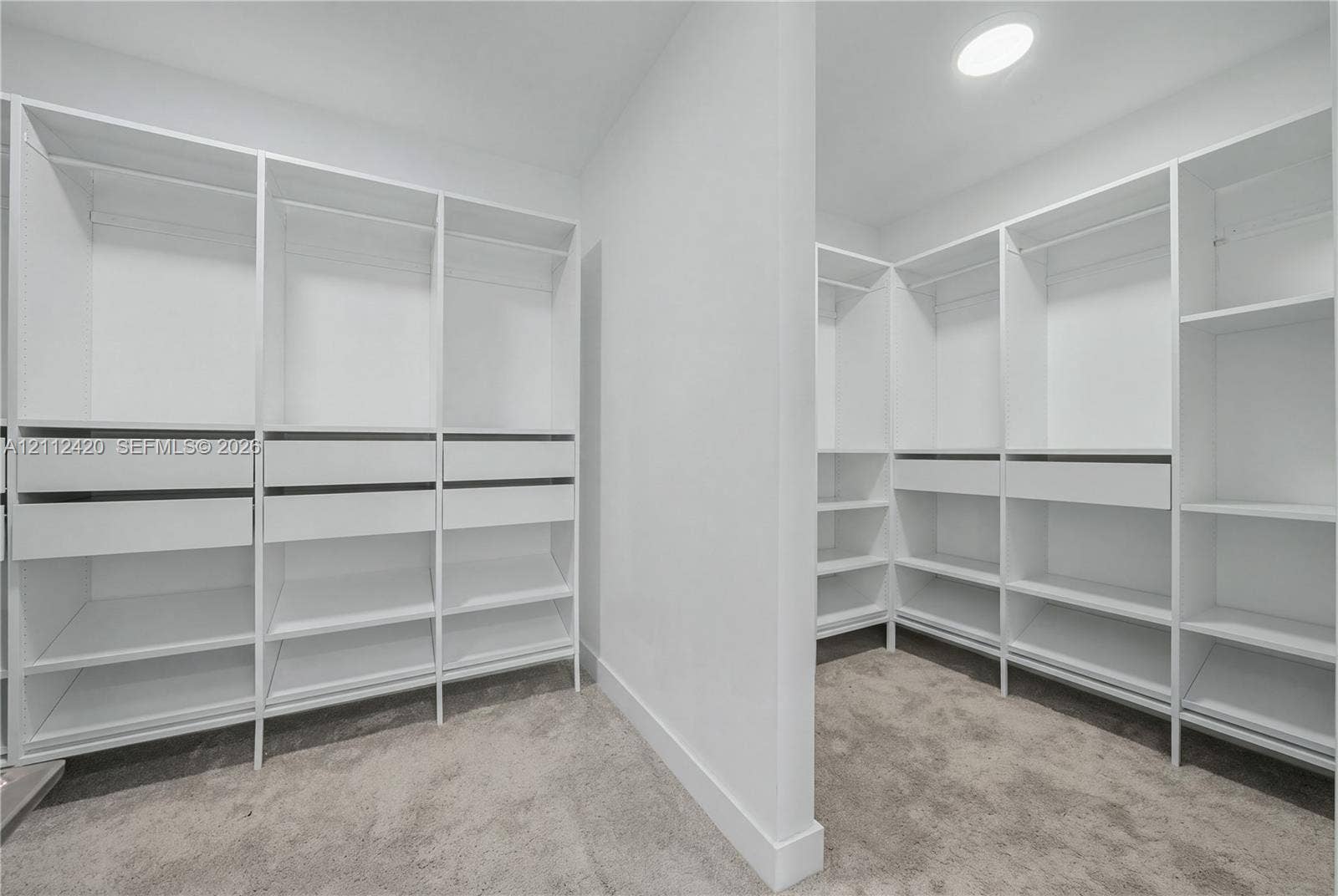 10054 NW 76th Terrace, Doral, FL 33178 Walk-in closet featuring white built-in shelving, integrated hanging rods, multiple storage drawers, and neutral carpeting