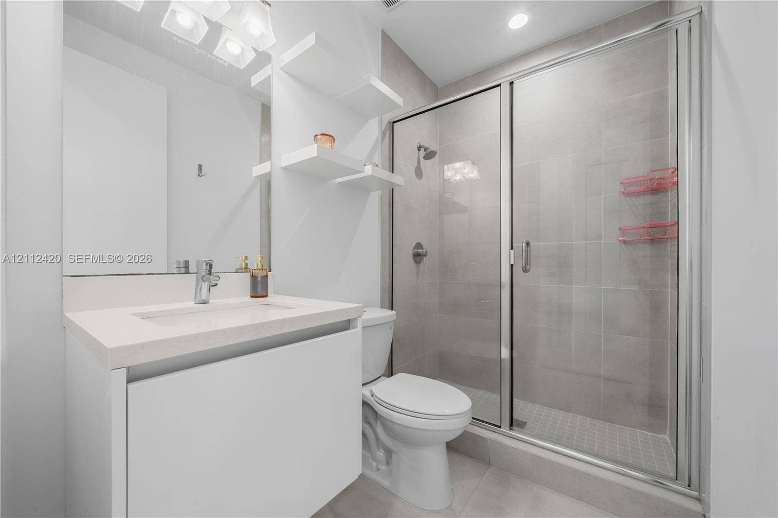 10054 NW 76th Terrace, Doral, FL 33178 Bathroom featuring a white vanity with a rectangular sink, quartz countertop, built-in wall shelving, and a tiled shower enclosure with a glass door