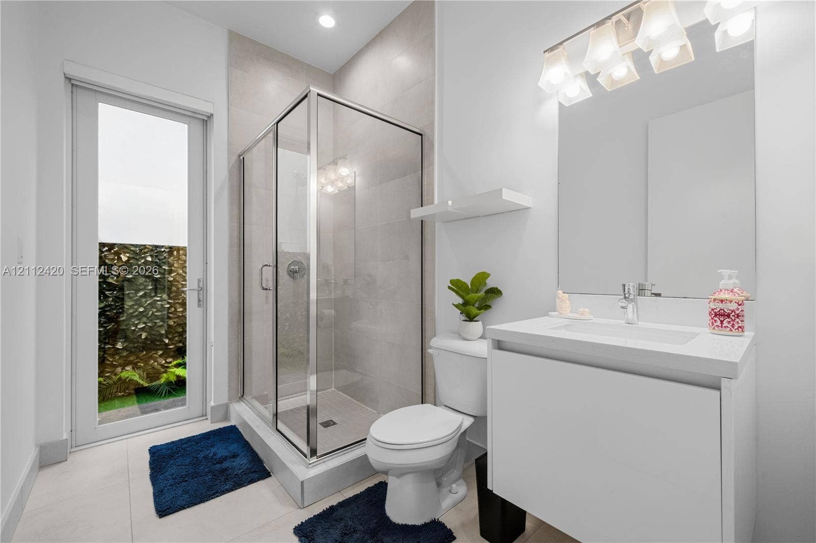 10054 NW 76th Terrace, Doral, FL 33178 Full-height tiled walk-in shower with glass enclosure, white floating vanity with integrated rectangular sink, stone-finish countertop, and glass-paneled exterior door