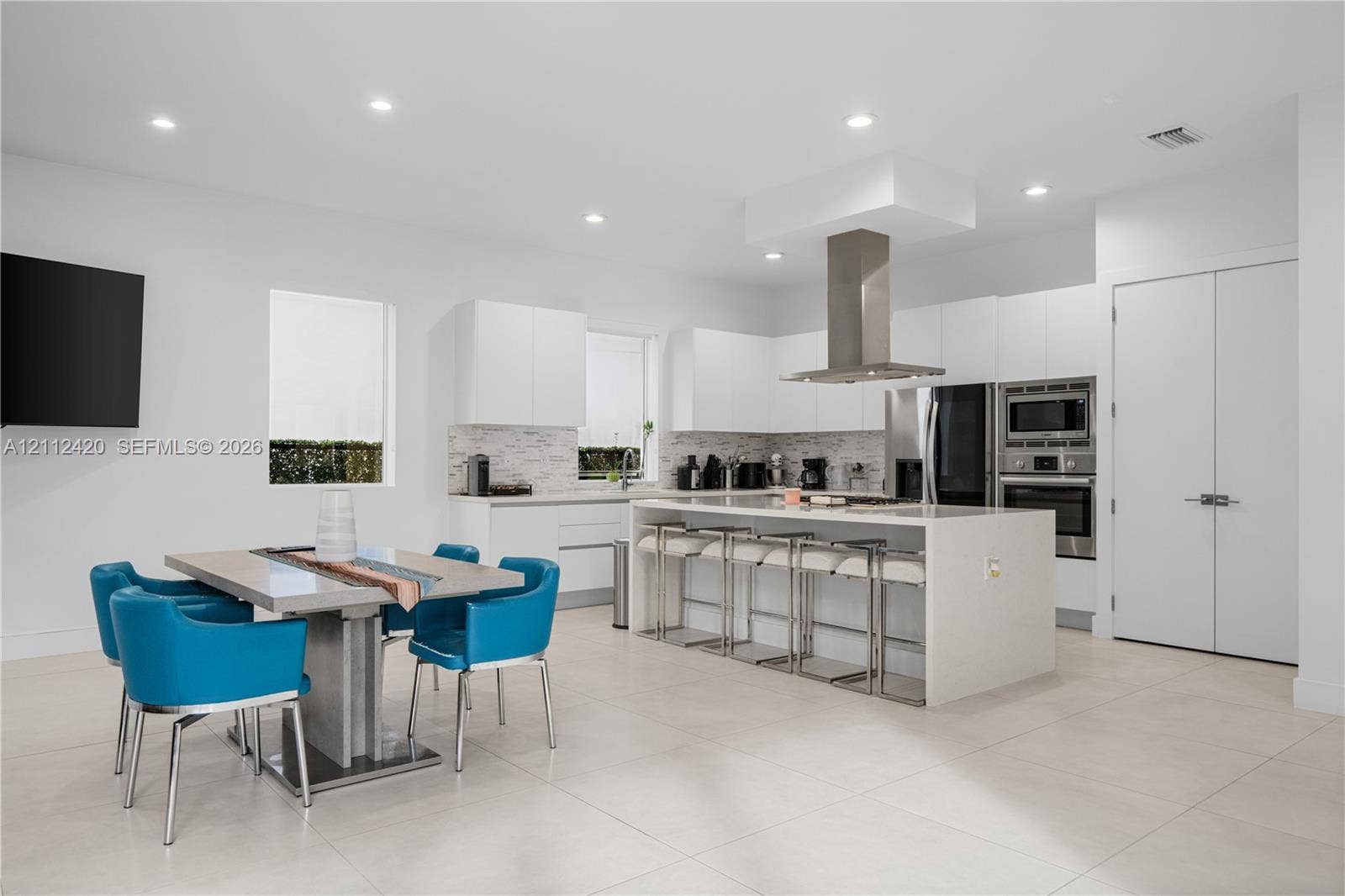 10054 NW 76th Terrace, Doral, FL 33178 Kitchen featuring flat-panel cabinetry, a quartz-topped center island with integrated seating, stainless steel appliances, a chimney-style range hood, and tile flooring