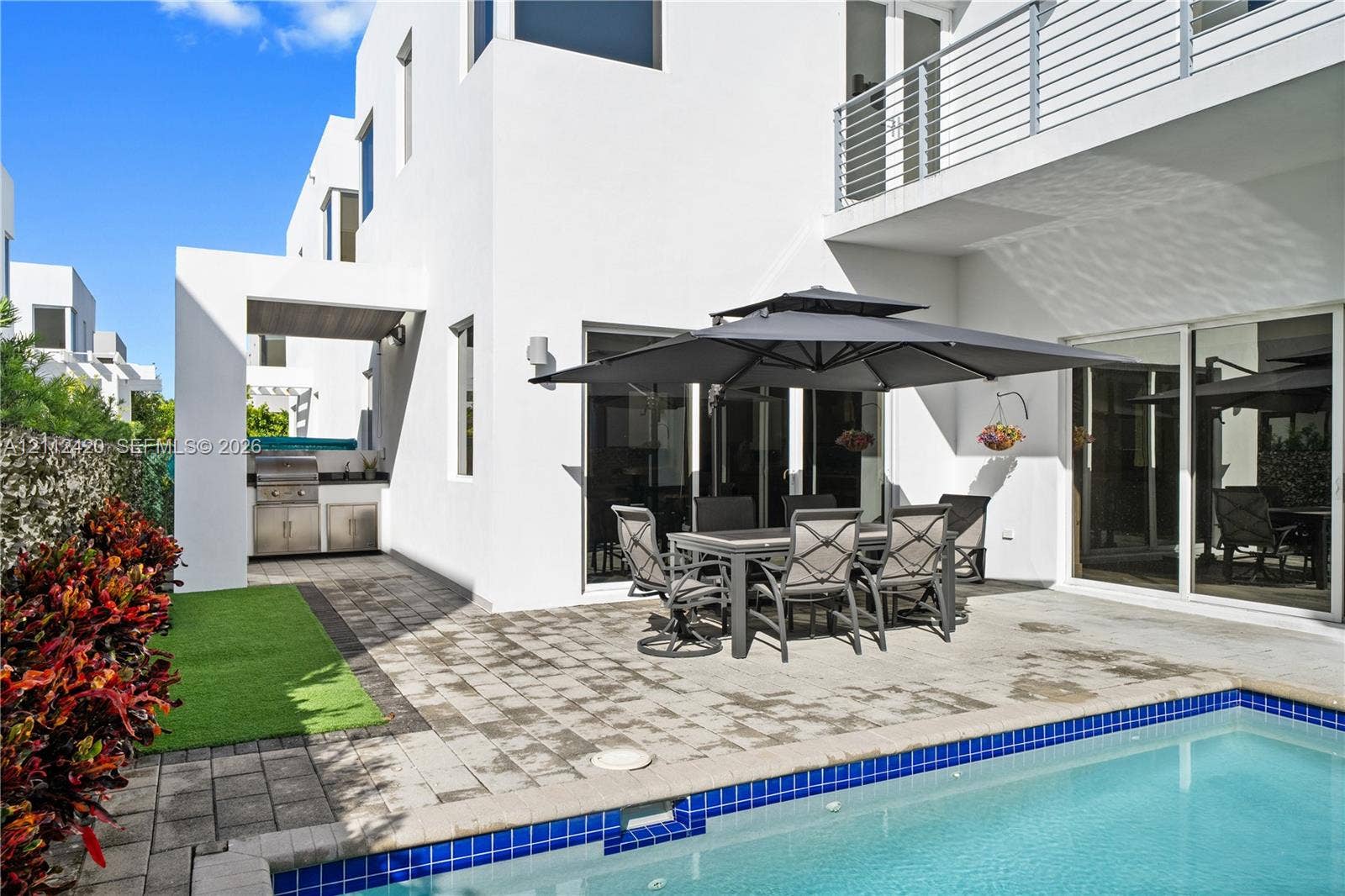10054 NW 76th Terrace, Doral, FL 33178 Modern exterior with a swimming pool, stone-paver patio, built-in outdoor kitchen, and a second-story balcony featuring metal railing