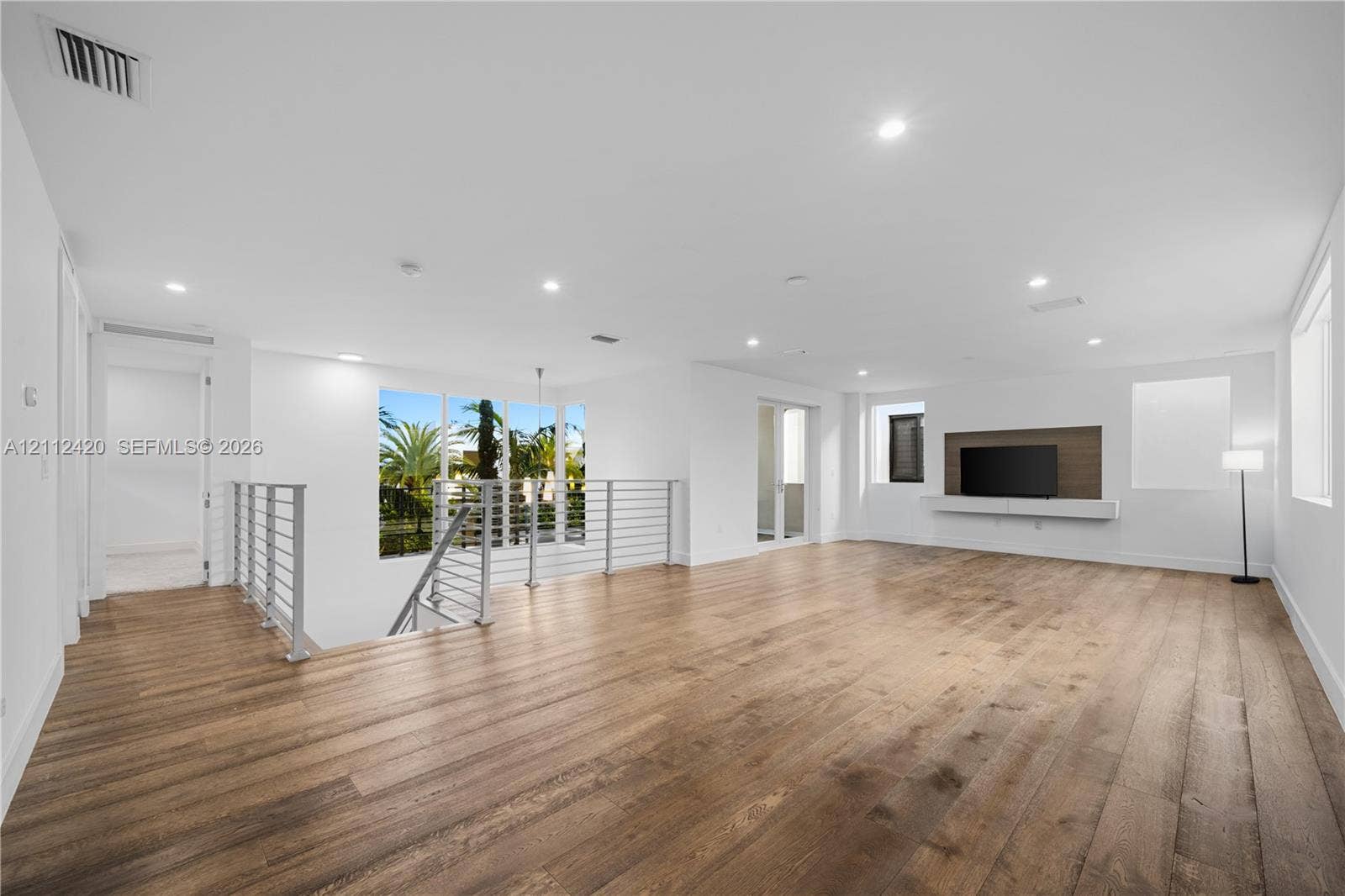 10054 NW 76th Terrace, Doral, FL 33178 Open-concept interior featuring wood-finish flooring, recessed lighting, a built-in media console, and a horizontal metal-railing staircase