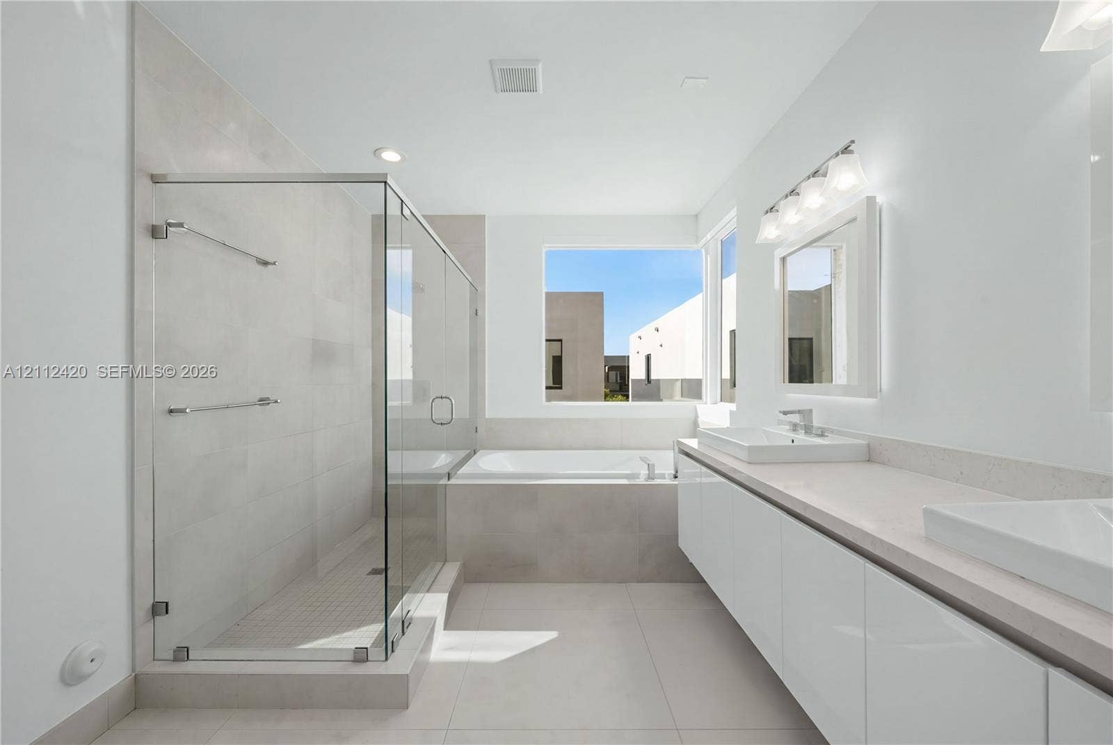 10054 NW 76th Terrace, Doral, FL 33178 Bathroom featuring a glass-enclosed walk-in shower with tiled surround, a built-in soaking tub, a long dual-sink vanity with light-tone countertops, and high-gloss white cabinetry