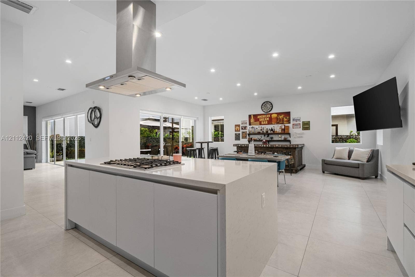 10054 NW 76th Terrace, Doral, FL 33178 Kitchen featuring a large central island with quartz countertops, built-in gas cooktop, stainless steel ventilation hood, and light-colored tile flooring