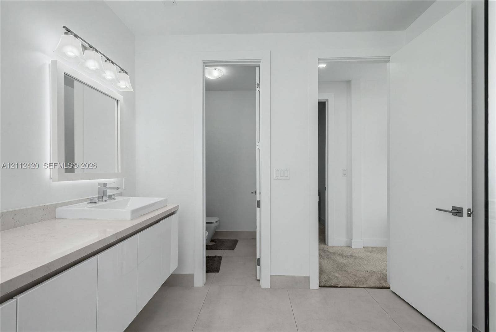 10054 NW 76th Terrace, Doral, FL 33178 Modern floating vanity with a rectangular sink, light-toned countertop, four-bulb vanity light, and large format floor tile