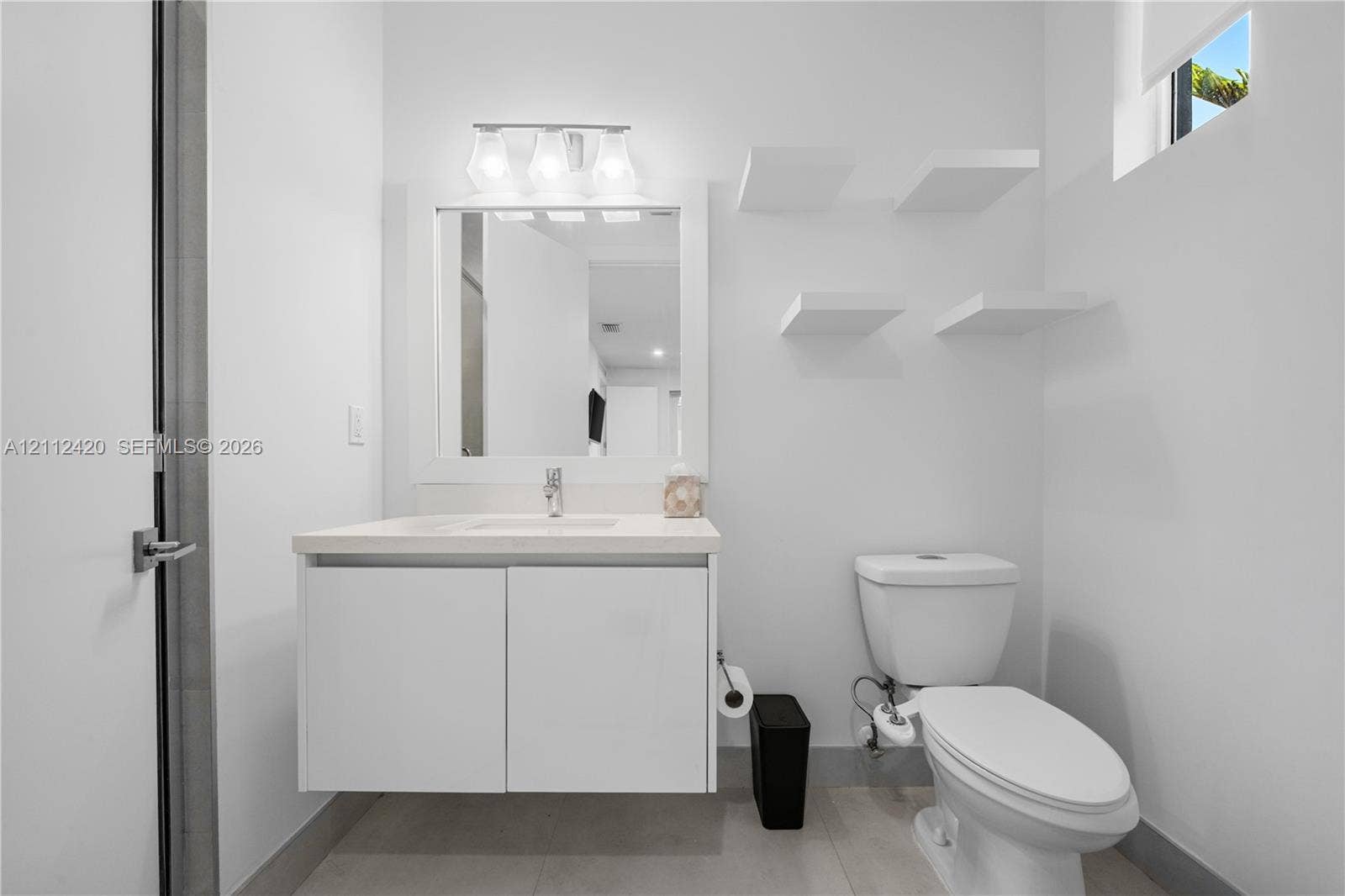 10054 NW 76th Terrace, Doral, FL 33178 Modern floating vanity with a solid-surface countertop and integrated sink, complemented by built-in wall shelving, a rectangular mirror, and a three-light fixture