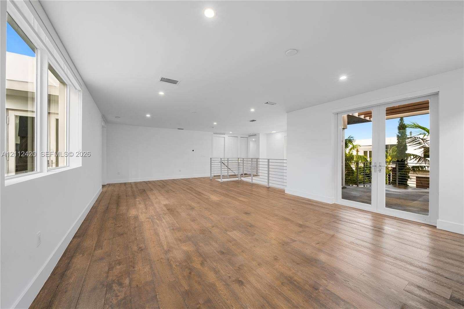 10054 NW 76th Terrace, Doral, FL 33178 Open floor plan interior featuring wood-finish flooring, recessed lighting, multi-pane windows, and a metal horizontal-bar railing, with glass-paned double doors providing outdoor access