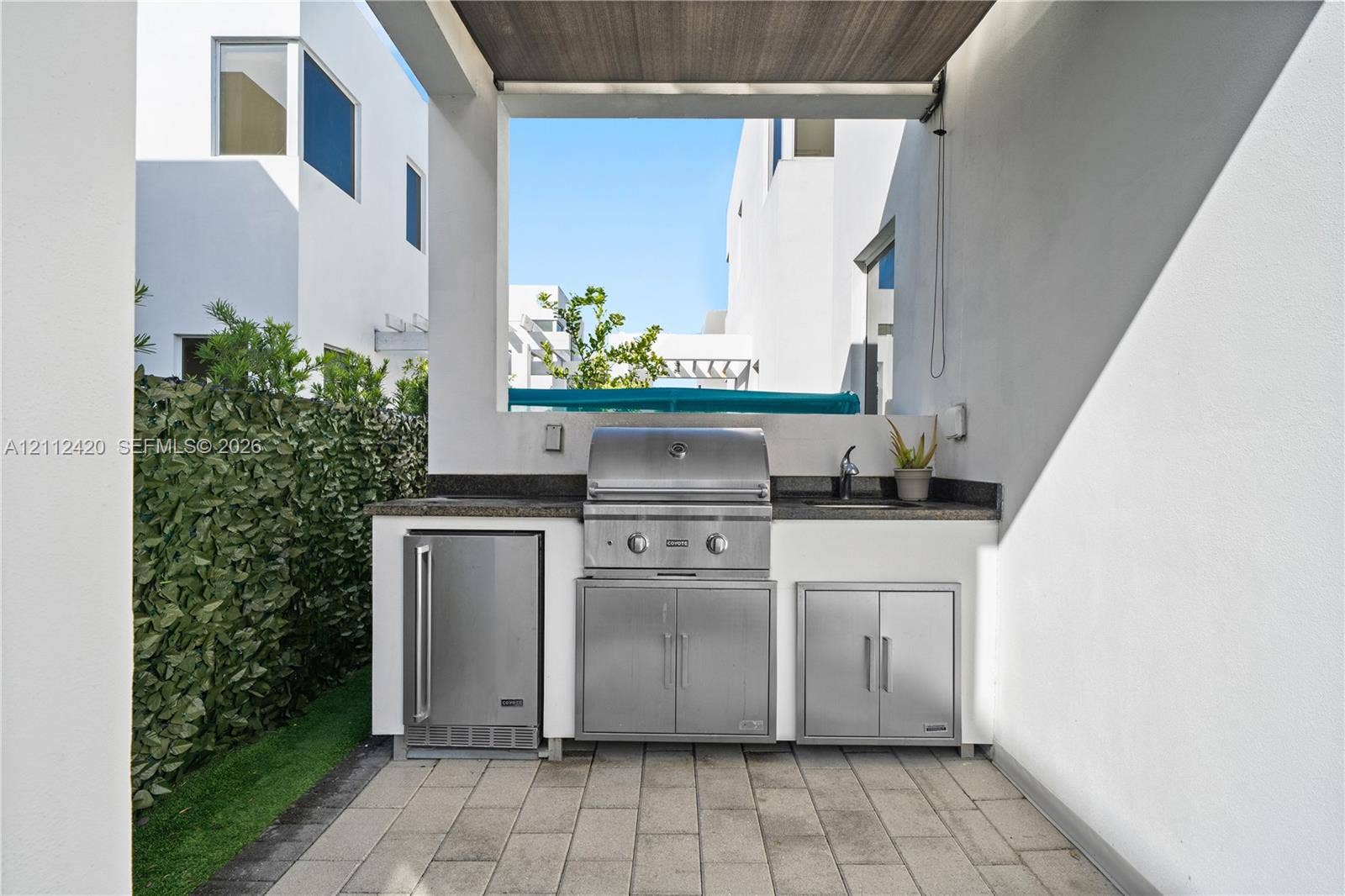 10054 NW 76th Terrace, Doral, FL 33178 Outdoor kitchen featuring a stone-topped counter, stainless steel grill, under-counter refrigeration, built-in cabinetry, and a prep sink, set upon a paved patio