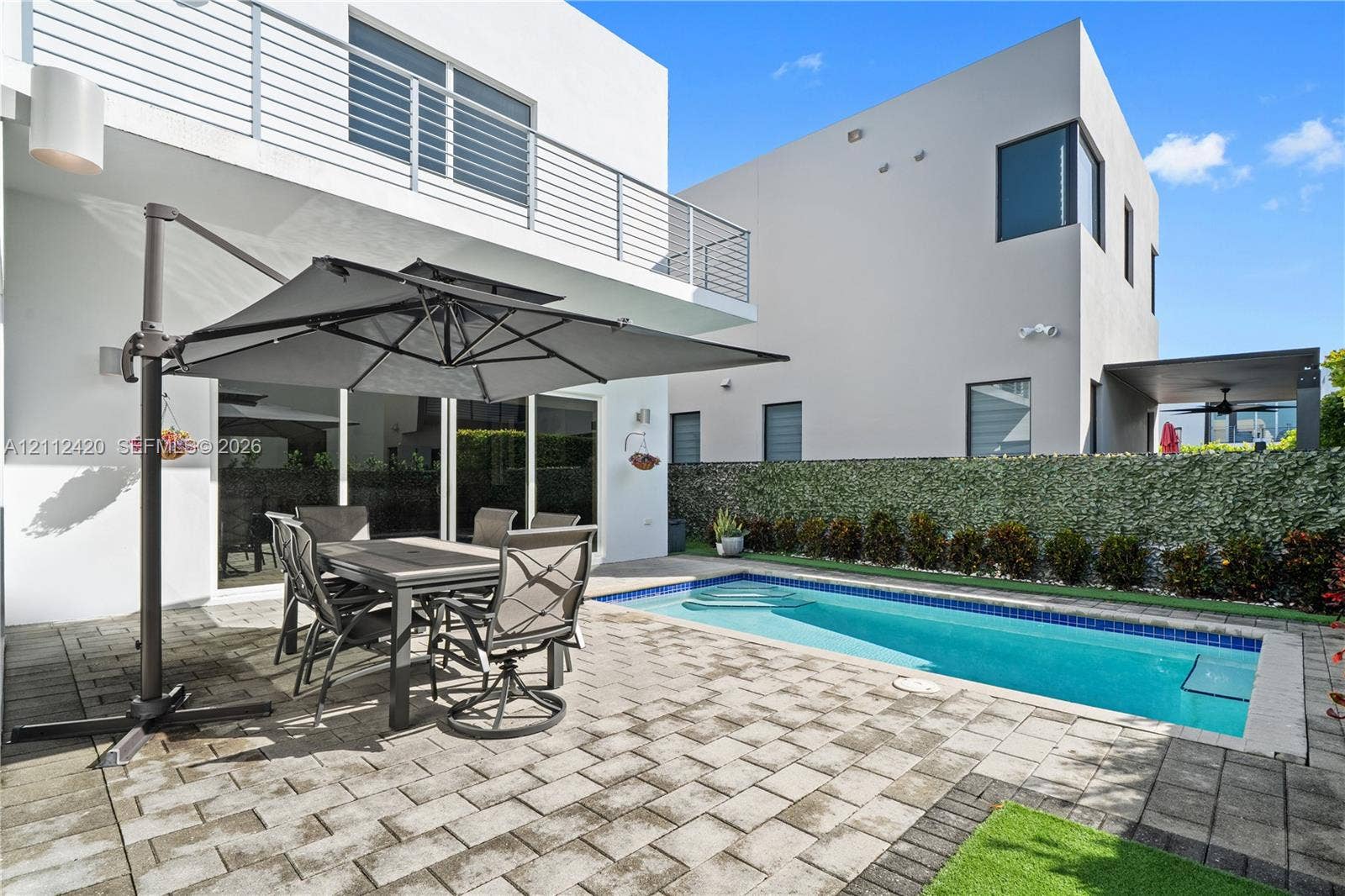 10054 NW 76th Terrace, Doral, FL 33178 Modern exterior featuring a paved stone patio, in-ground swimming pool, horizontal metal balcony railing, and floor-to-ceiling sliding glass doors