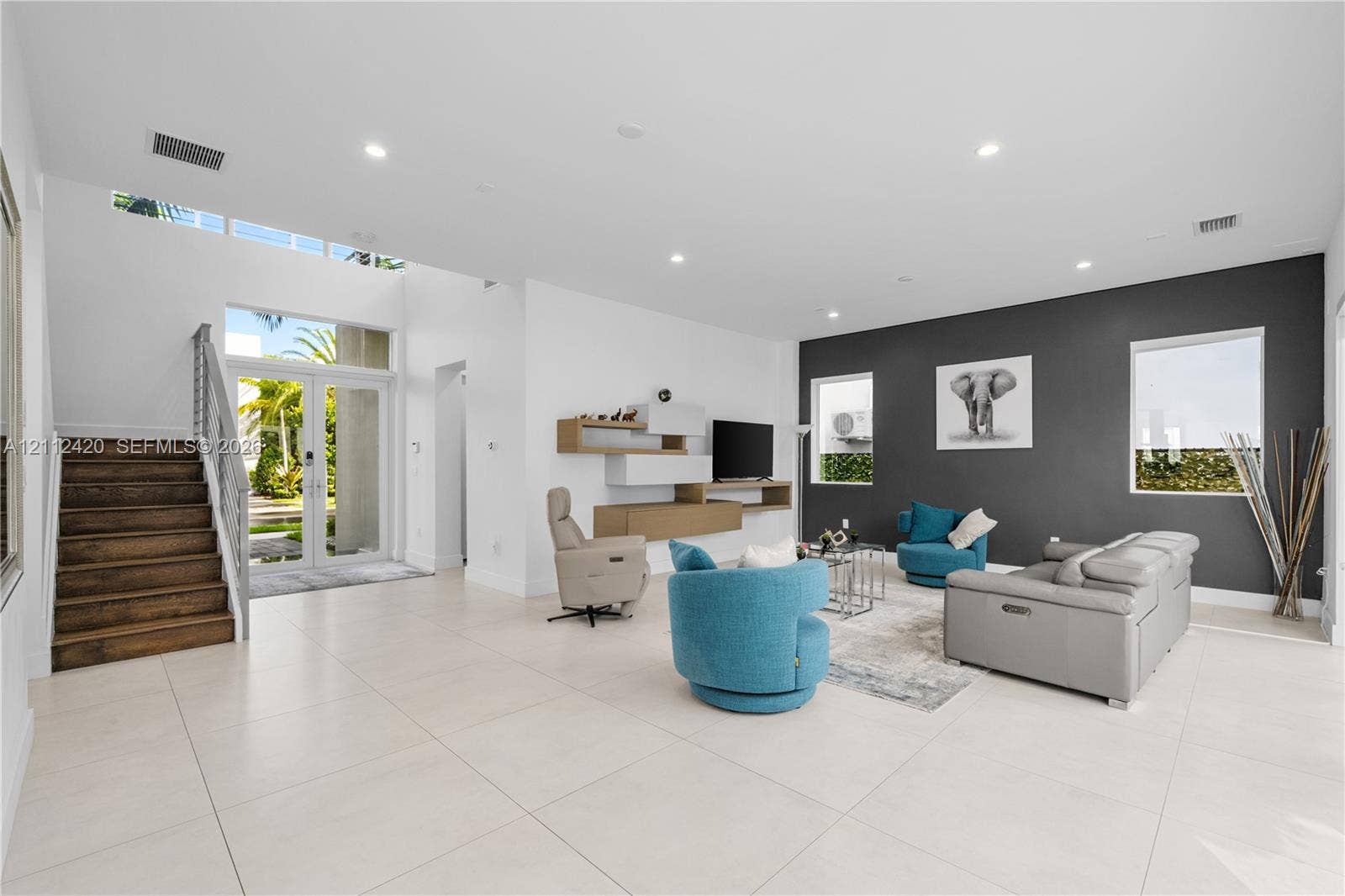 10054 NW 76th Terrace, Doral, FL 33178 High-ceiling open interior featuring large-format tile flooring, a charcoal accent wall, recessed lighting, and a staircase with wood-finish treads