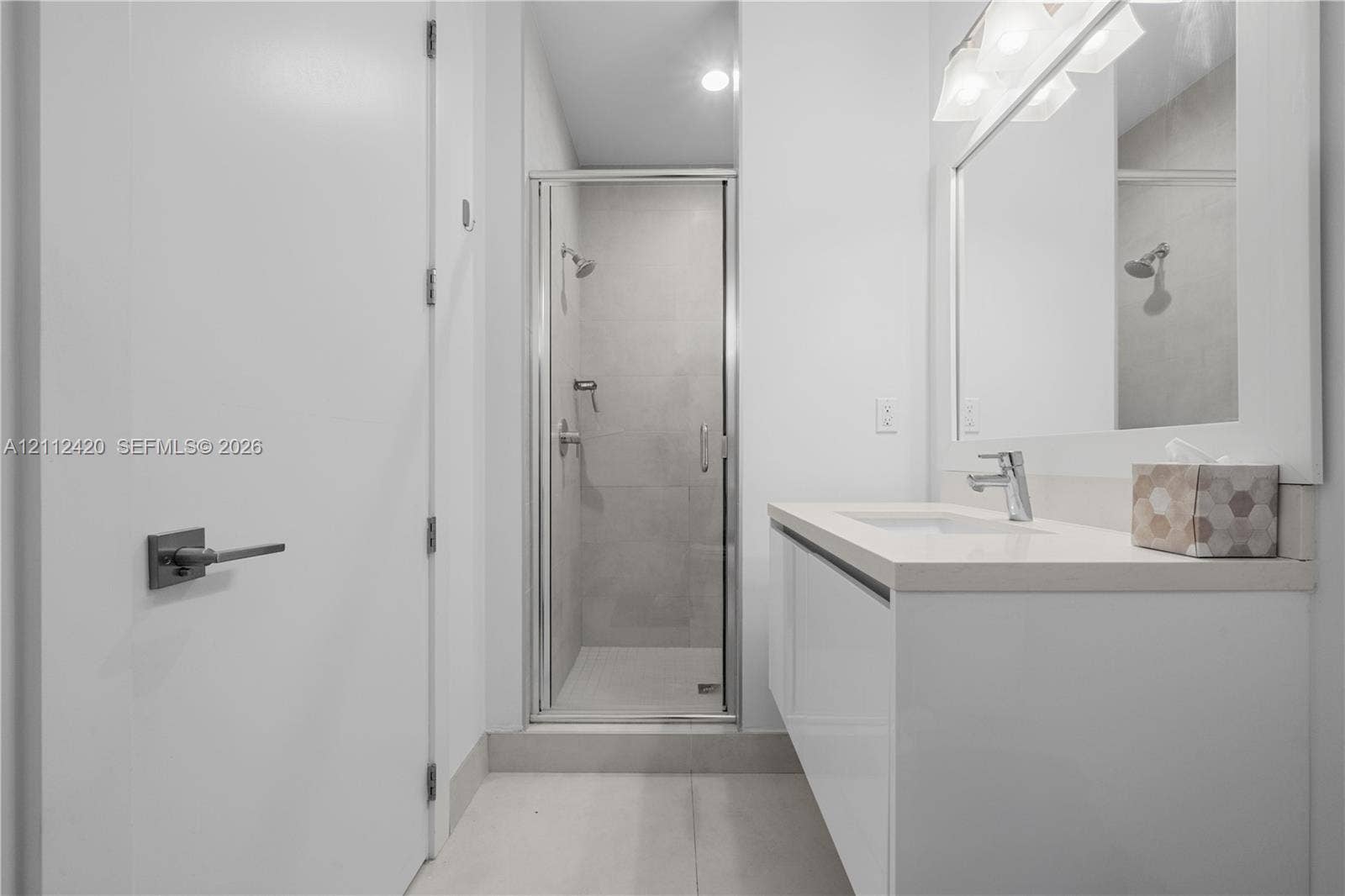 10054 NW 76th Terrace, Doral, FL 33178 Modern vanity featuring a stone countertop and integrated sink, chrome faucet, framed mirror with mounted lighting, and a glass-enclosed shower with tiled walls
