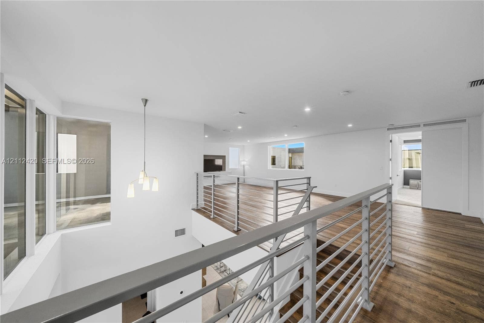 10054 NW 76th Terrace, Doral, FL 33178 Open-concept interior featuring wood-finish flooring, a multi-light pendant fixture, horizontal metal railing system, and recessed lighting