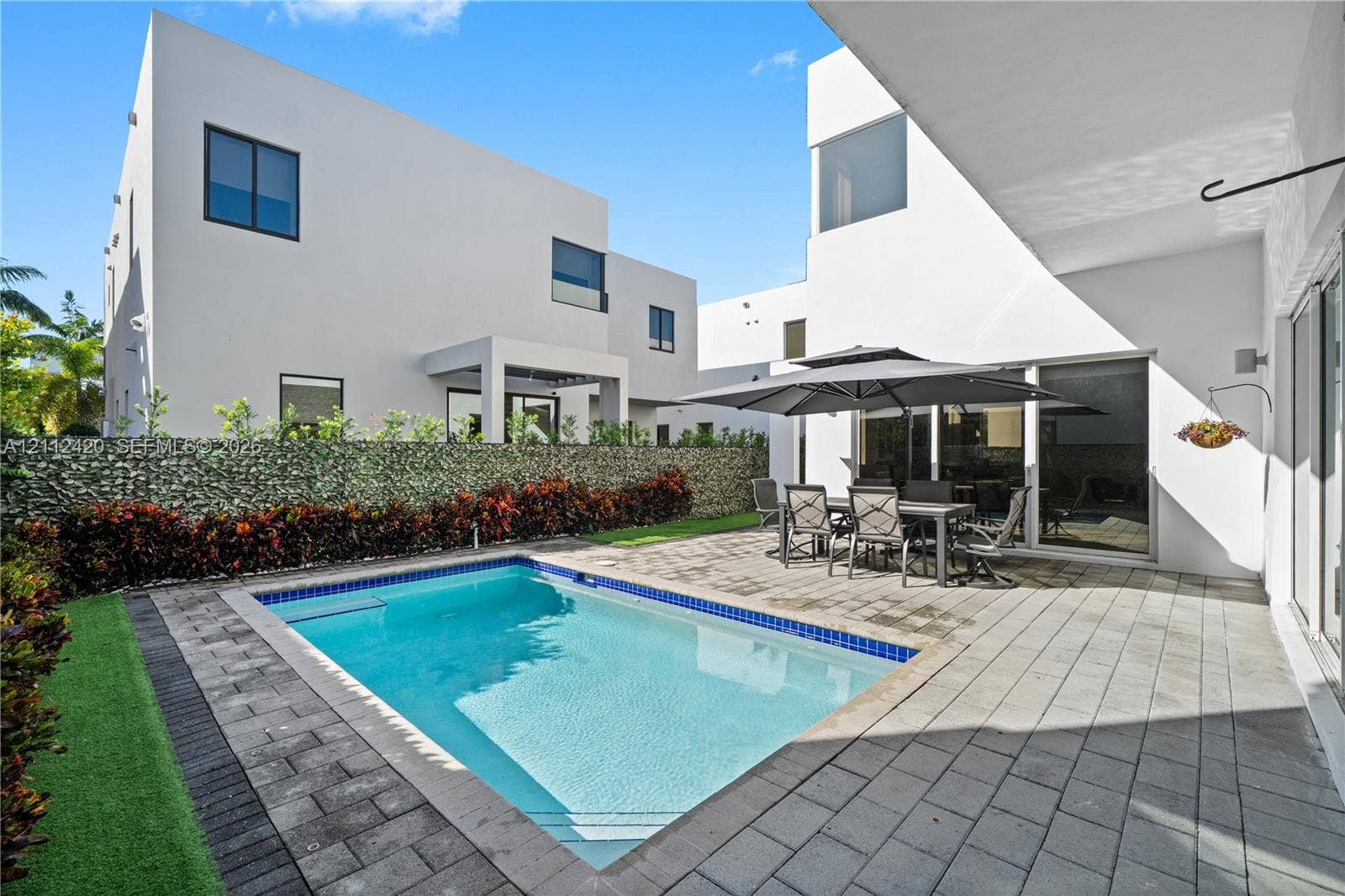 10054 NW 76th Terrace, Doral, FL 33178 In-ground swimming pool with a tiled perimeter, expansive stone-paver patio, and perimeter wall with integrated greenery