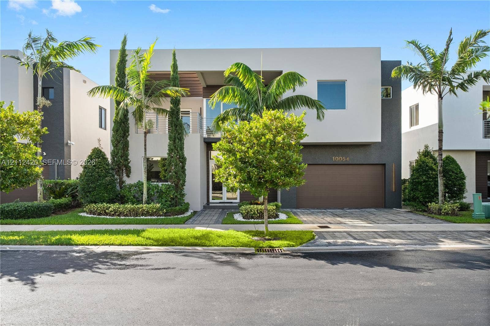 10054 NW 76th Terrace, Doral, FL 33178 Contemporary two-story exterior featuring a smooth stucco finish, attached two-car garage with solid door, second-level balcony with metal railing, and paver driveway