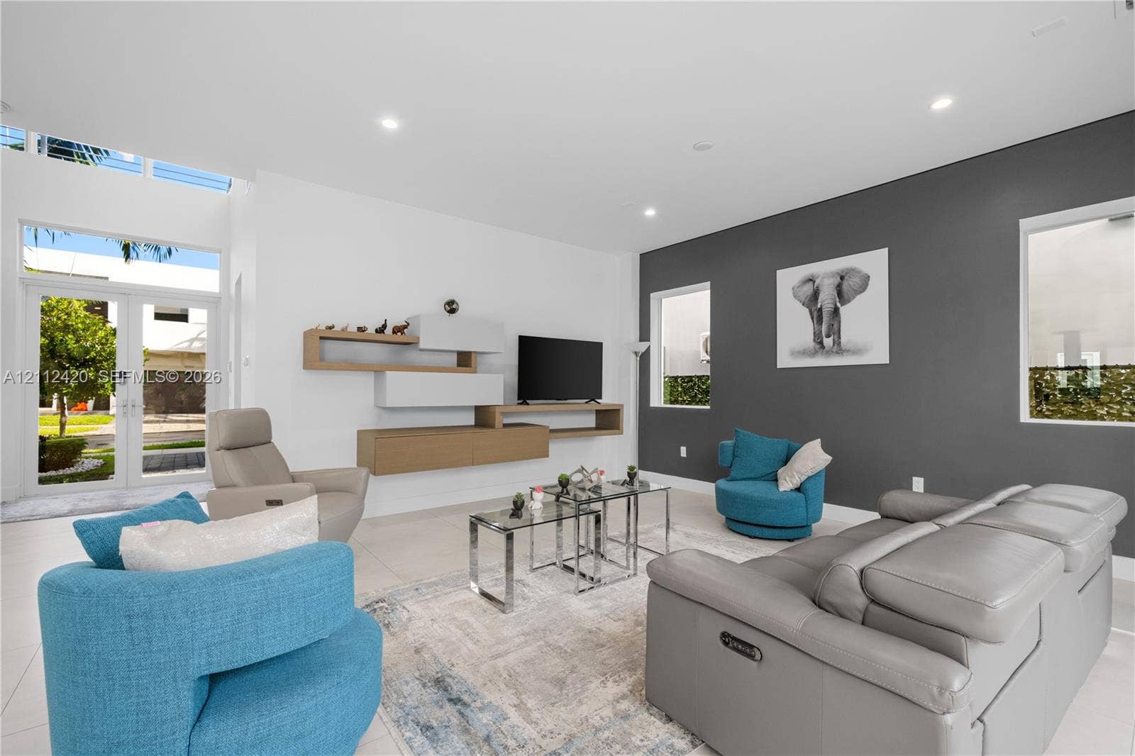 10054 NW 76th Terrace, Doral, FL 33178 Living area featuring high ceilings, large-format tile flooring, a custom wall-mounted storage unit, recessed lighting, and an accent wall with windows