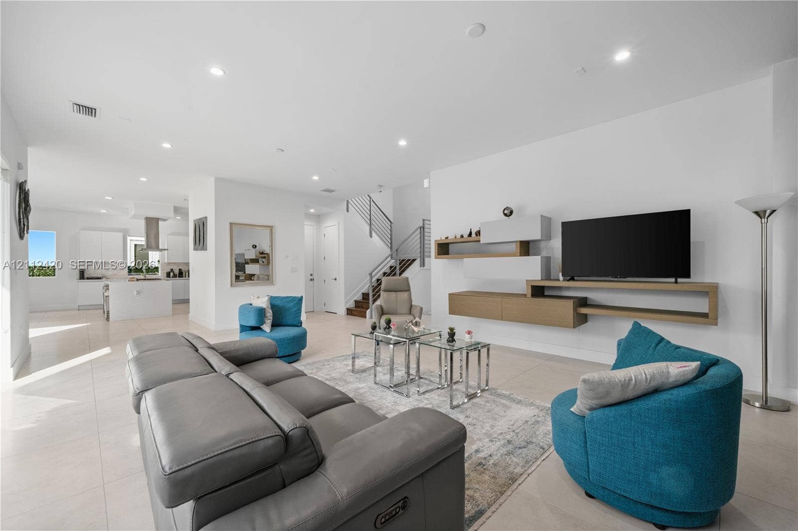10054 NW 76th Terrace, Doral, FL 33178 Open-concept living space featuring large-format tile flooring, recessed lighting, wall-mounted floating cabinetry, and a staircase with metal horizontal railings