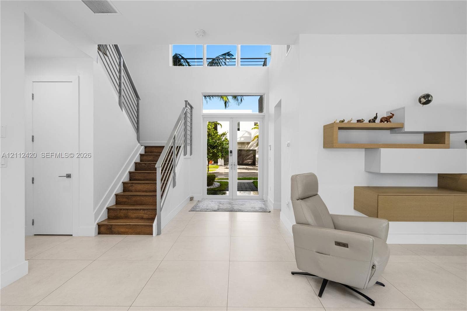 10054 NW 76th Terrace, Doral, FL 33178 Entryway featuring a double-height ceiling, glass-paneled double front doors, transom windows, a staircase with wood treads and horizontal metal railings, and built-in wall-mounted cabinetry