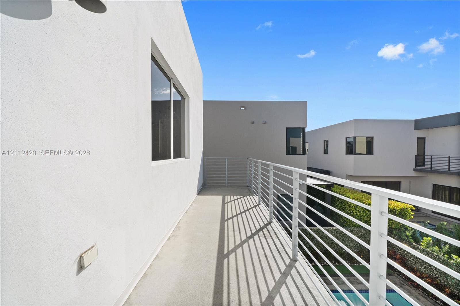 10054 NW 76th Terrace, Doral, FL 33178 Modern balcony featuring white stucco exterior walls, horizontal slat metal railing, and smooth concrete flooring