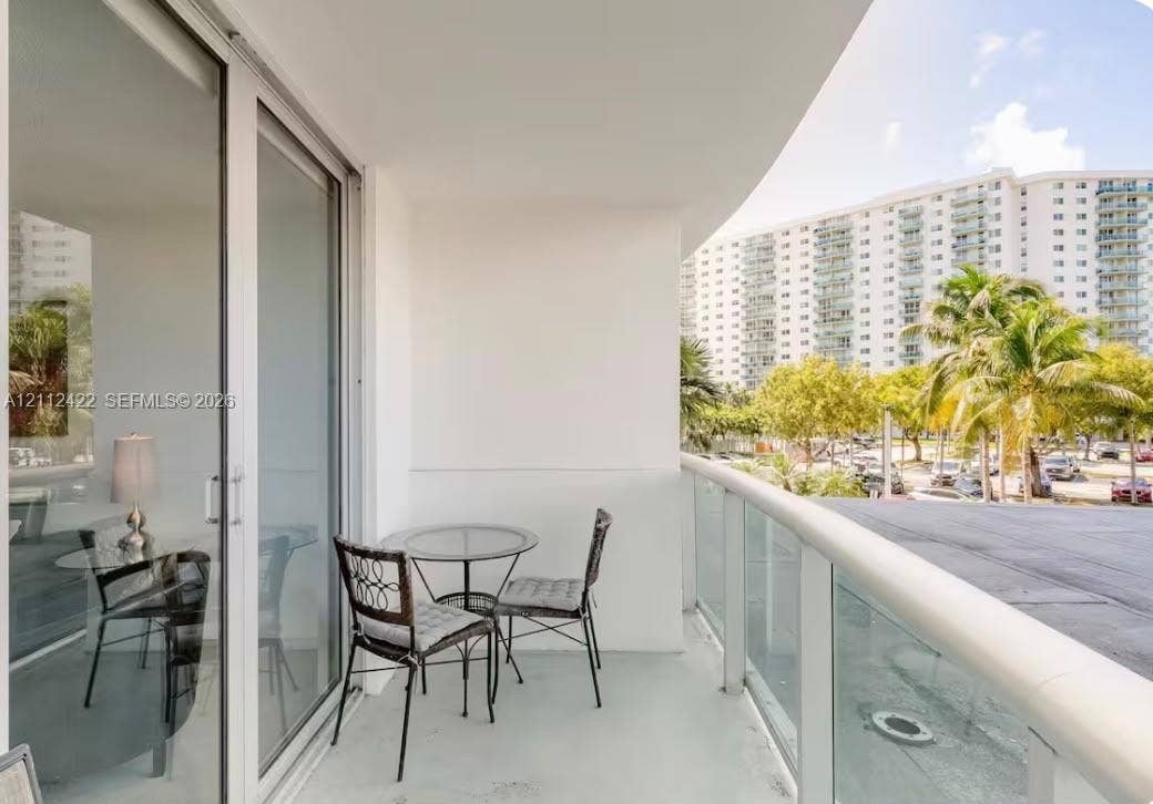 Covered balcony featuring a glass panel railing, painted concrete flooring, and sliding glass door access