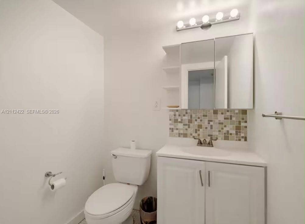 White vanity with integrated basin, multicolor mosaic tile backsplash, mirrored medicine cabinet with integrated shelving, and five-bulb vanity light fixture