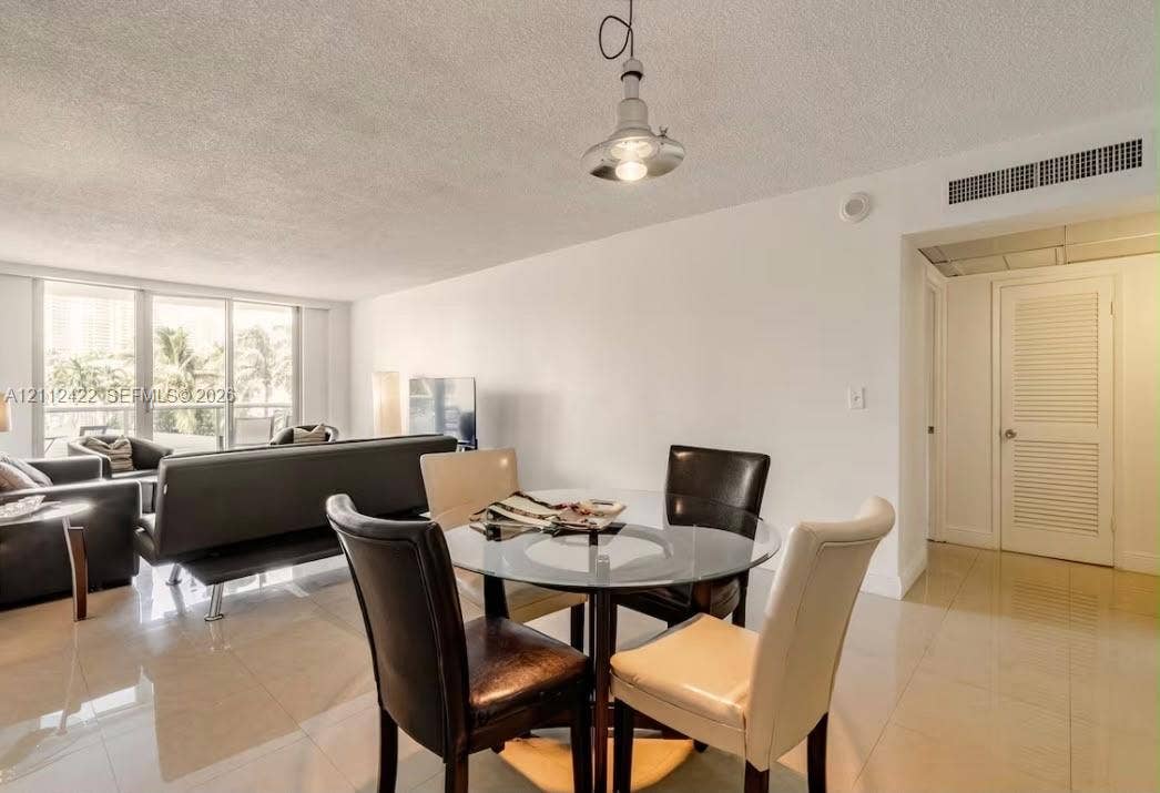 Living area featuring large-format tile flooring, floor-to-ceiling glass sliding doors, a metal pendant light fixture, and a louvered closet door