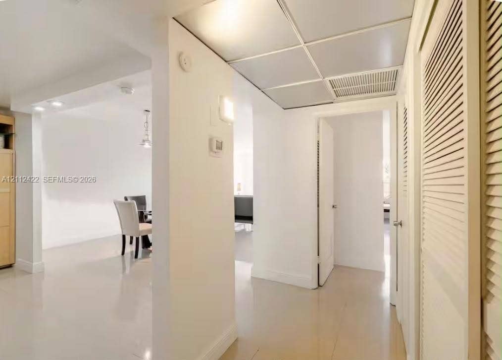 Interior hallway featuring glossy tile flooring, recessed ceiling grid panels, and built-in louvered-style closet doors
