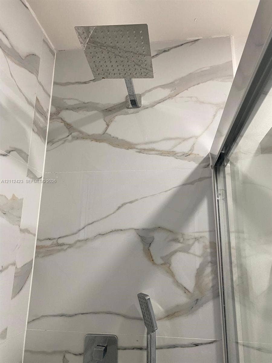 8555 SW 152nd Avenue, #104, Miami, FL 33193 Walk-in shower featuring large-format wall tile with veining, a rainfall showerhead, a handheld shower wand, and a glass door enclosure