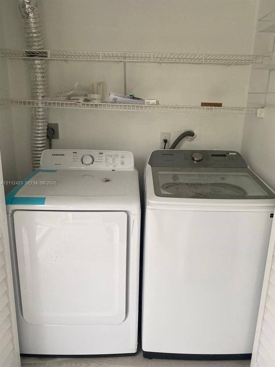 8555 SW 152nd Avenue, #104, Miami, FL 33193 Laundry closet featuring side-by-side washer and dryer units with dual-level white wire shelving