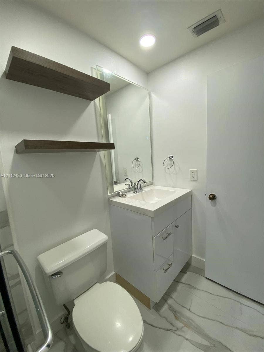 8555 SW 152nd Avenue, #104, Miami, FL 33193 Modern vanity featuring a white cabinet, integrated sink, and chrome faucet, complemented by wall-mounted wood-finish floating shelves, a large wall mirror, and stone-finish tile flooring