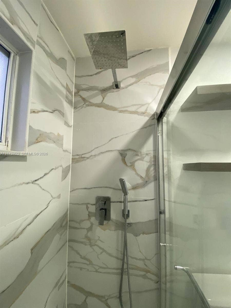 8555 SW 152nd Avenue, #104, Miami, FL 33193 Shower enclosure featuring large-format veined tile surround, overhead rainfall showerhead, wall-mounted handheld sprayer, and built-in shelving