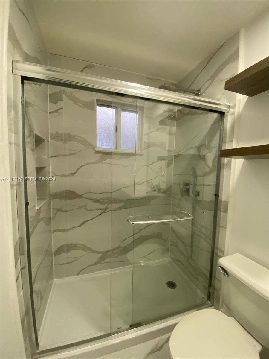 8555 SW 152nd Avenue, #104, Miami, FL 33193 Walk-in shower enclosure featuring floor-to-ceiling veined tile surround, recessed wall niche, sliding glass doors, built-in shelving, and polished metal hardware