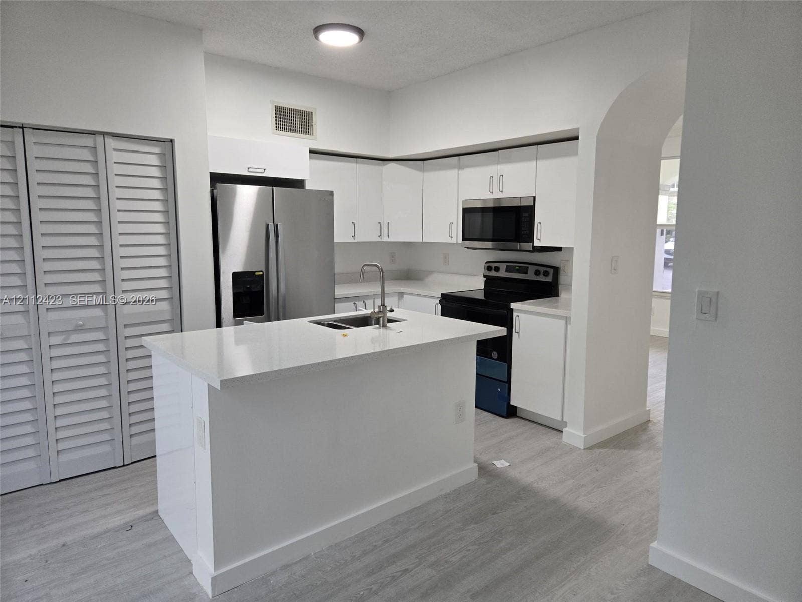 8555 SW 152nd Avenue, #104, Miami, FL 33193 Kitchen featuring white shaker-style cabinetry, an island with an integrated stainless steel sink, stone-finish countertops, stainless steel refrigerator, and wood-finish flooring