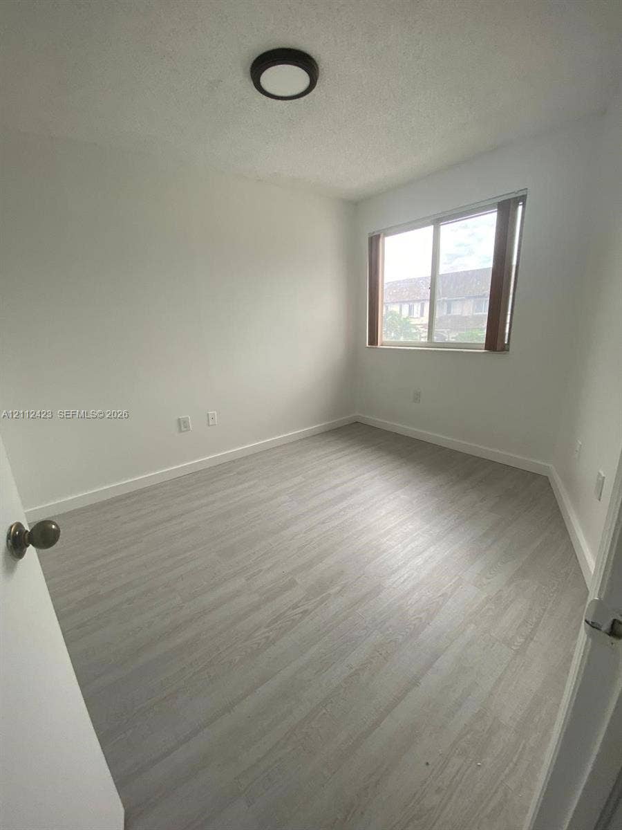 8555 SW 152nd Avenue, #104, Miami, FL 33193 Room featuring light-toned wood-finish flooring, a sliding window with neutral trim, and a low-profile flush-mount ceiling light