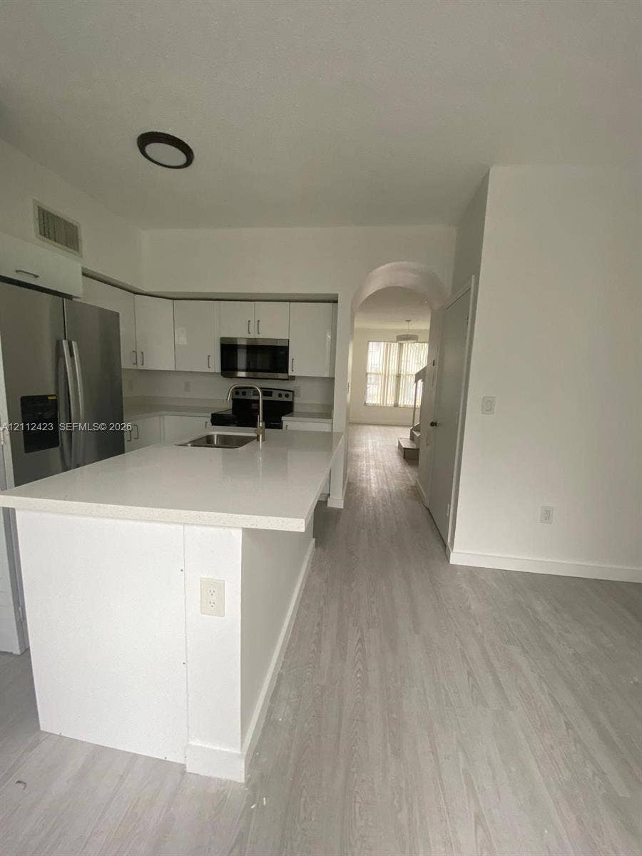 8555 SW 152nd Avenue, #104, Miami, FL 33193 Kitchen featuring a stone-surface island, stainless steel refrigerator, flat-panel white cabinetry, wood-finish flooring, and an arched entry