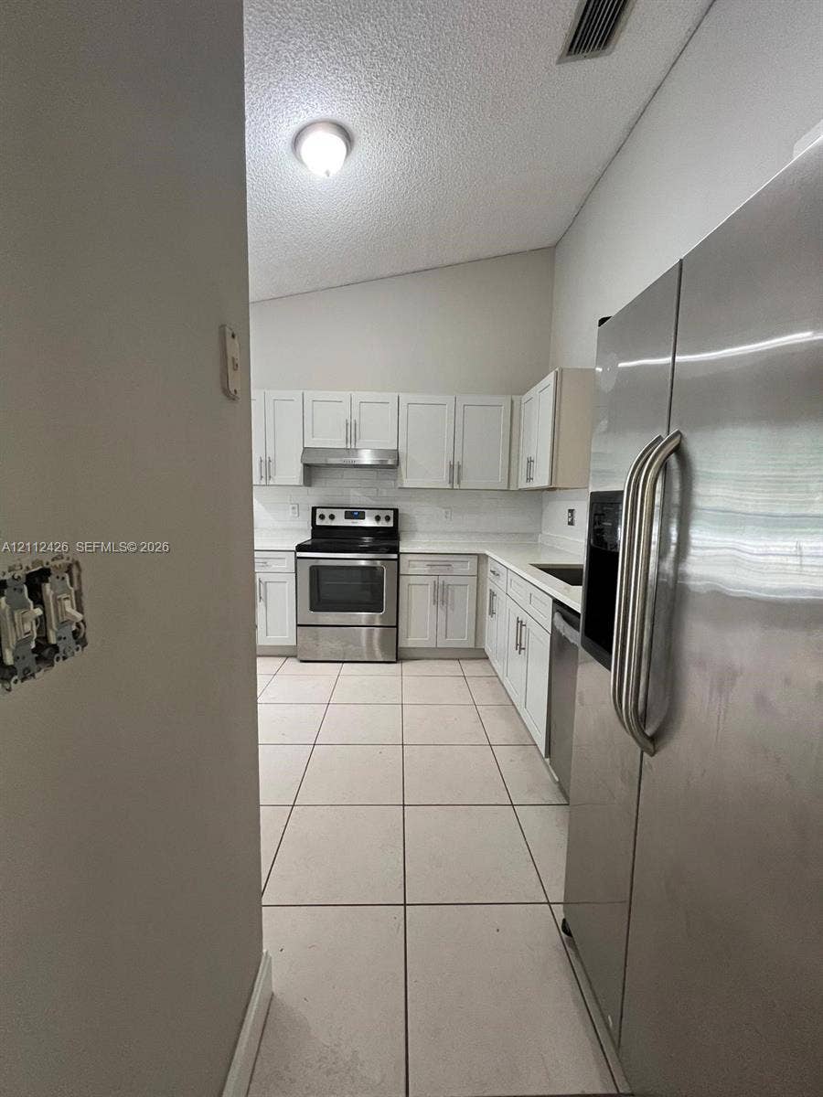 Kitchen featuring white cabinetry, solid-surface countertops, stainless steel appliances, and tile flooring under a vaulted ceiling