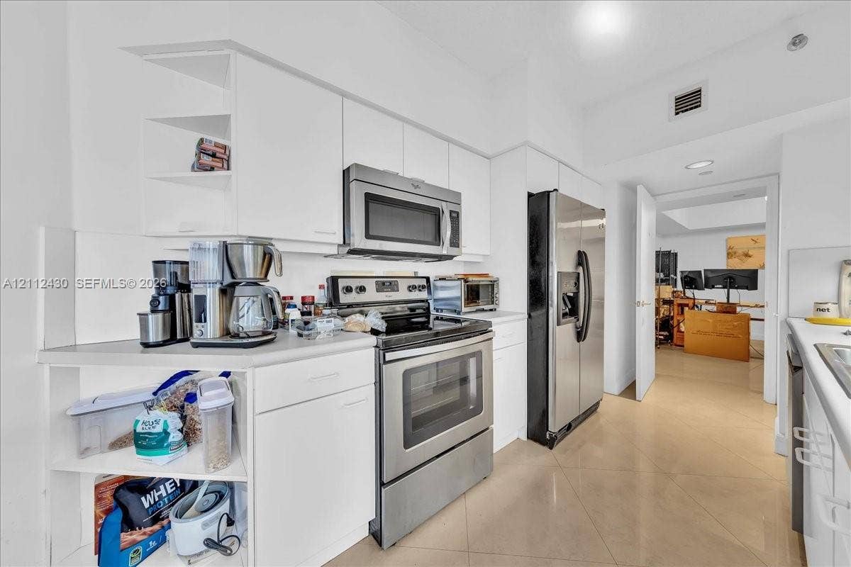 Kitchen featuring white cabinetry, stainless steel appliances, and tile flooring