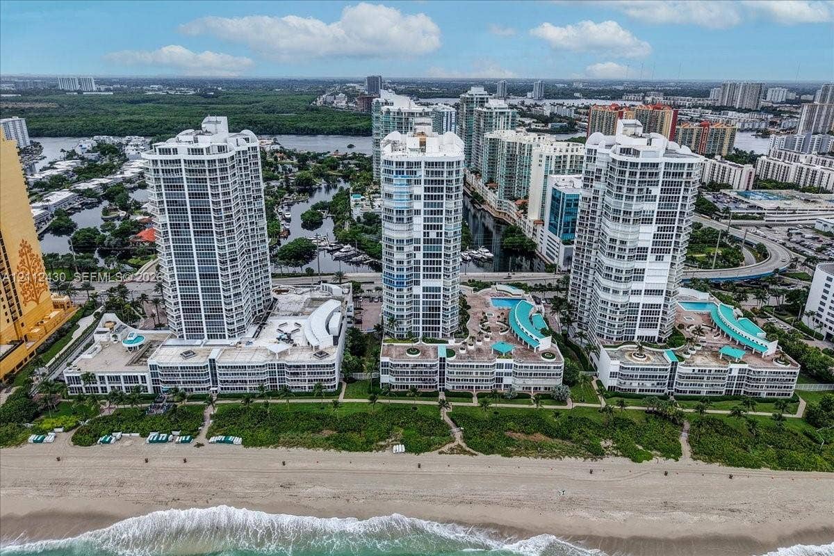 High-rise residential complex featuring beachfront access, podium-level swimming pools, tiered structural design, and glass-paneled balconies