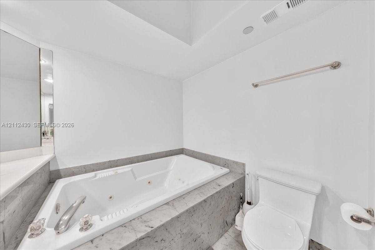 Built-in jetted tub with a tiled surround, chrome faucet hardware, and wall-mounted towel bar