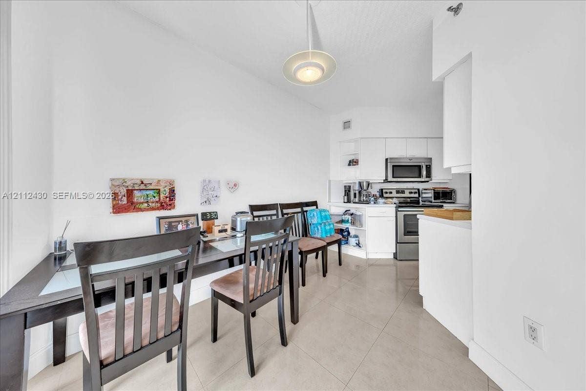 Kitchen area featuring white cabinetry, stainless steel appliances, large-format tile flooring, and a contemporary pendant light fixture